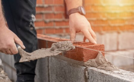 Téléchargez les photos : Maçonnerie maçonnerie brique sur mélange de ciment sur chantier de construction close-up. Réduire la crise du logement en construisant des maisons plus abordables concept - en image libre de droit