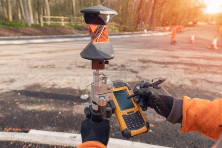 Photo for Site engineer operating his touch screen controller instrument during roadworks. Builder using touch screen controller to control total positioning station tachymeter on construction site for new road setting out - Royalty Free Image