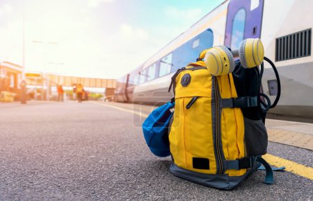 Mochila amarilla con auriculares y gorra en la plataforma en una estación de tren. Concepto turístico de viaje. luz de viaje