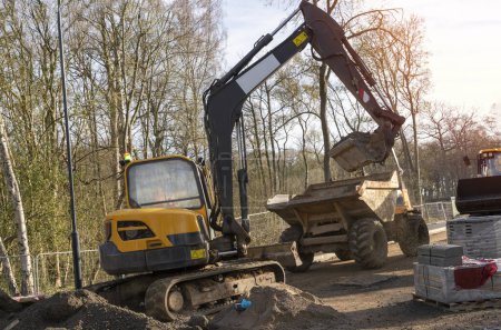 Foto de Excavadora cargando mezcla de hormigón semi-seco en el vertedero en el sitio de construcción - Imagen libre de derechos
