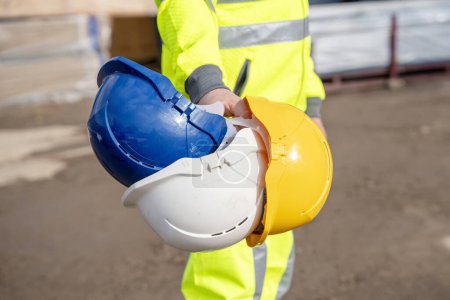 Photo for A builder wearing a hi-viz reflective suit gives a choice of helmets. Always use safety and personal protective equipment for building site personnel, engineer and construction workers. Always use correct PPE on the construction site concept - Royalty Free Image