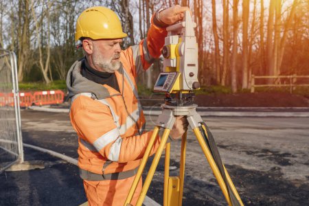 Photo for Site engineer setting his instrument during roadworks. Builder installing total positioning station tachymeter on construction site for new road setting out - Royalty Free Image