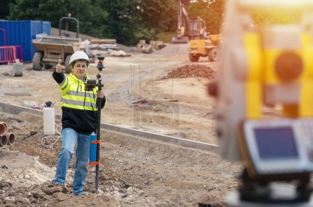 Téléchargez les photos : Ingénieur de chantier femme travaillant avec l'équipement EDM de la station totale de théodolite sur un chantier de construction à l'extérieur - en image libre de droit