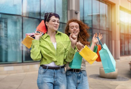 Téléchargez les photos : Les femmes avec des sacs colorés s'amuser avec des achats dans la ville urbaine. Consommation, vente, achats, achats, mode de vie concept. - en image libre de droit