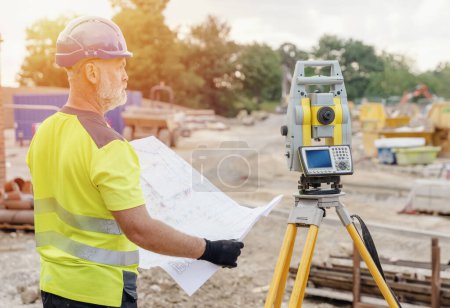 Téléchargez les photos : Un homme ingénieur de chantier arpenteur travaillant avec la station totale de théodolite équipement EDM sur un chantier de construction à l'extérieur - en image libre de droit