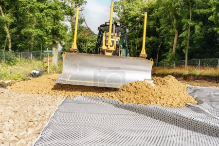 Roadworks and bulldozer levelling stone on top of geogrid plastic mesh