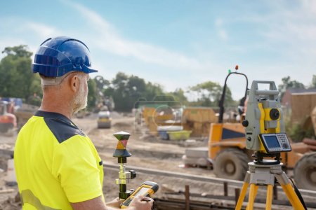 A man site engineer surveyor working with theodolite total station EDM equipment on a building construction site outdoors