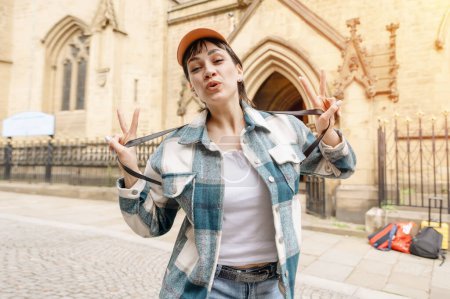 Foto de Mujer en camisa azul y gorra con mochila caminando por la ciudad, tomando fotos, selfie, divirtiéndose como concepto de estilo de vida turístico - Imagen libre de derechos