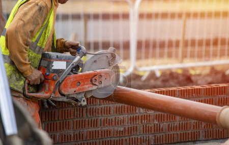 Téléchargez les photos : Groundworker builder coupe tuyau de drainage sale en plastique à l'aide d'une scie à essence close-up - en image libre de droit