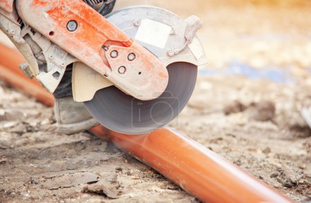 Groundworker builder cutting plastic foul drainage pipe using a petrol-powered saw close-up