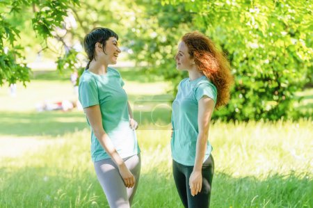 Zwei fröhliche junge Freundinnen trafen sich im Park bei Sportübungen und hielten für einen kurzen Plausch inne.
