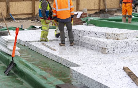 Builder placing polystyrene insulation boards on waterproofing membrane during floor construction. Energy saving concept