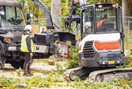 Arborist using a wood chipper machine for shredding trees and branches. The tree surgeon is wearing a safety helmet with a visor and ear protectors