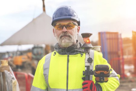 Closeup portrait of a Surveyor builder site engineer with theodolite total station at construction site outdoors during surveying work