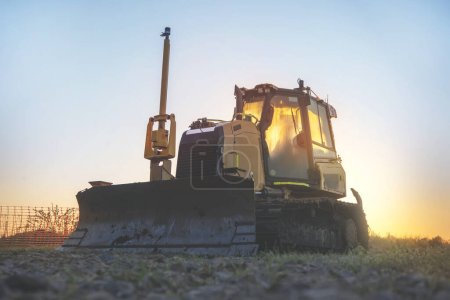 Silhouette d'un bulldozer sur un chantier de construction tôt le matin contre le ciel bleu et l'image tonique du soleil levant