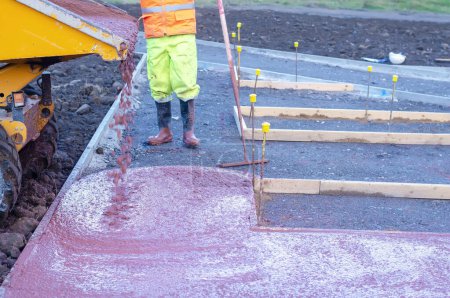 Les constructeurs versant et nivelant le béton prêt à l'emploi humide dans le coffrage lors de la construction de nouveaux sentiers