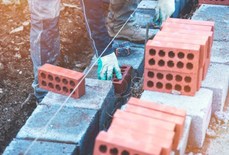 Fleißige Maurer verlegen Betonklötze auf Betonfundamente auf einem neuen Wohnbaugebiet. Kampf gegen Wohnungsnot durch mehr bezahlbare Wohnungen