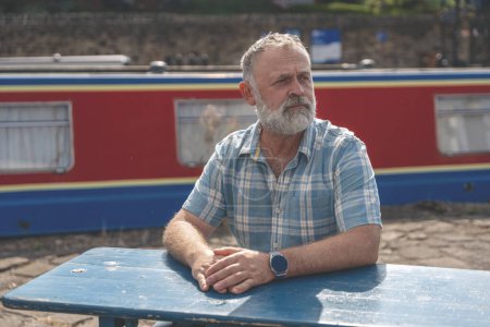a mature bearded man sitting  on a bench, walking at a quay, enjoying warm days of the spring, summer