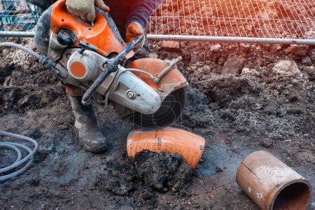 Bauarbeiter schneidet Tonrohr mit Benzinbetonsäge und Diamantklinge