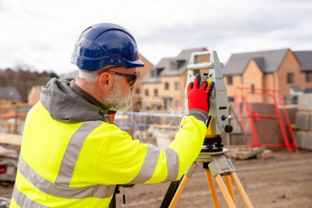 Surveyor builder site engineer with theodolite total station at construction site outdoors during surveying work