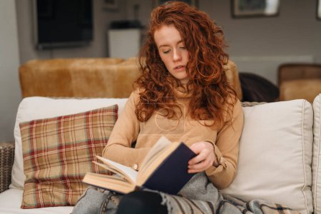 a beautiful redhead girl reading a book, concepts of home and comfort