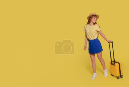 eine fröhliche junge Frau in blauem Rock, gelbem T-Shirt und Hut, die einen Koffer auf gelbem Grund trägt. Glückliche Menschen im Urlaub, Urlaub