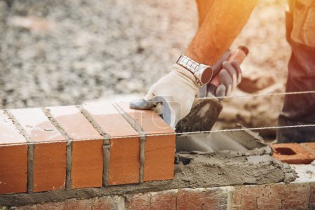 Industrial bricklayer laying bricks on cement mix on construction site close-up