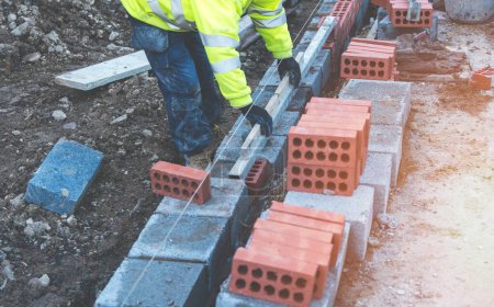 Hard working bricklayer laying concrete blocks on top of concrete foundation on new residential housing site. Fight housing crisis by building more affordable houses concept