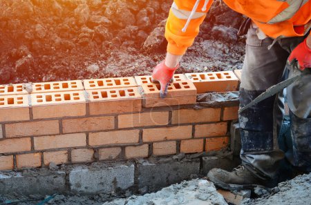 Téléchargez les photos : Industrial bricklayer laying bricks on cement mix on construction site. Fighting housing crisis by building more affordable houses concept - en image libre de droit