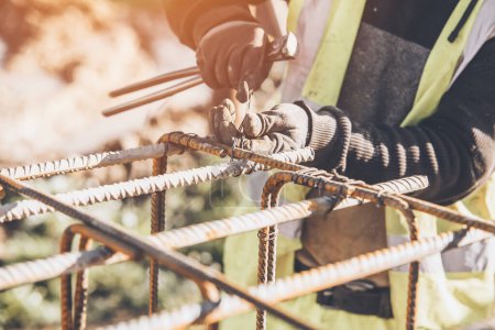 A worker uses steel tying wire to fasten steel rods to reinforcement bars close-up. Reinforced concrete structures - making a steel reinforcing cage for concrete beam