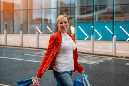 glückliche Frau in roter Jacke mit bunten Taschen, die Spaß beim Einkaufen in der Großstadt hat. Konsum, Verkauf, Einkauf, Einkaufen, Lifestylekonzept