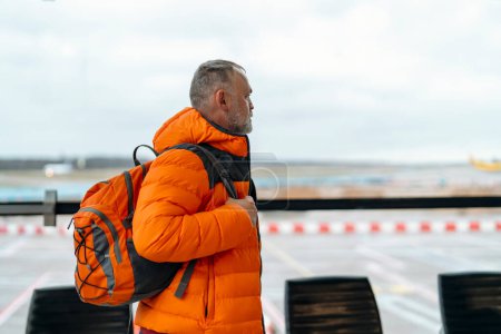 Reisende, die ein Telefon benutzen, auf einem Flughafen sitzen, auf einen Flug warten, einen Flughafen betreten und einen Rucksack bei sich tragen. Reisekonzept.