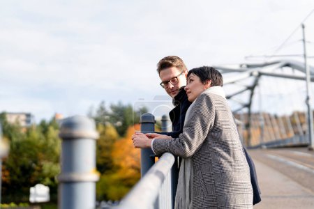 Hombre guapo y mujer hermosa enamorándose, abrazándose, mirando desde un puente mientras caminan alrededor de una ciudad, divirtiéndose, foto de estilo de vida