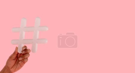 Frau mit Schild-Hashtag in der Hand auf rosa Hintergrund mit Kopierraum. Soziale Medien, Blogging und virale Themen im Internet-Konzept