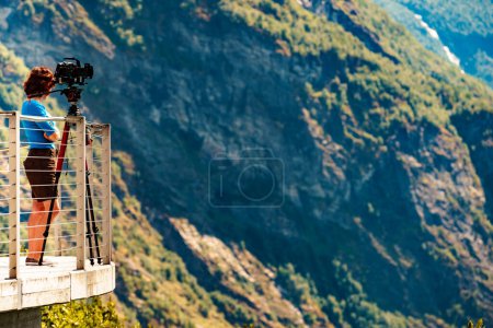 Téléchargez les photos : Touriste féminine avec appareil photo sur trépied prendre des photos de voyage, profiter des montagnes paysage de Ornesvingen plate-forme d'observation, Norvège. - en image libre de droit