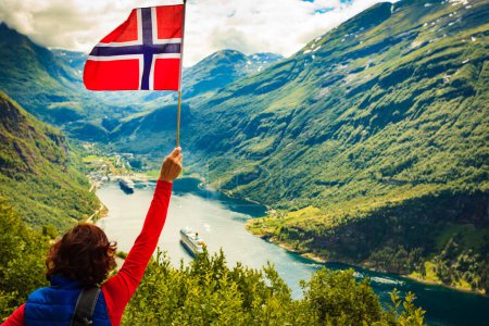 Téléchargez les photos : Touriste féminine avec drapeau nordique bénéficiant d'une vue panoramique sur le fjord Geirangerfjord avec bateau de croisière. Croisière vacances et voyage
. - en image libre de droit