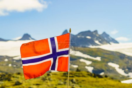 Téléchargez les photos : Drapeau norvégien agitant contre un paysage montagneux enneigé, été. Route touristique nationale Sognefjellet. - en image libre de droit