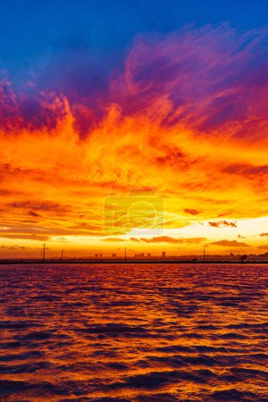 Brennender Sonnenuntergang über dem Meer. Abendliche Küstenlandschaft mit Stadtsilhouette. San Pedro del Pinatar, Murcia Spanien.