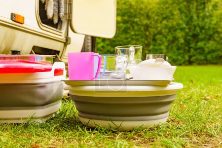 Many clean dishes drying outdoor against camper vehicle. Washing up on fresh air. Camping on nature, dishwashing outside.