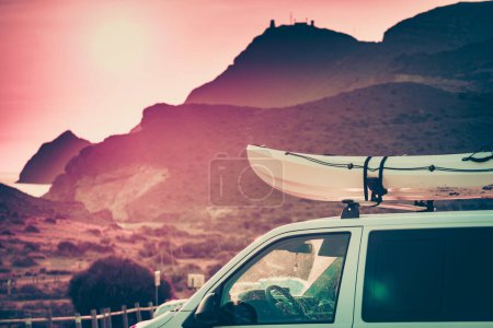 Car van with canoe on top roof against mountain nature at sunset. Cabo de Gata Nijar Natural Park, province Almeria, Andalusia in Spain. Active lifestyle.
