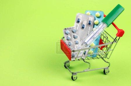 Photo for Thermometer, pills, tablets and vitamins in a shopping cart on green background. Concept: shopping and delivery of medicines - Royalty Free Image