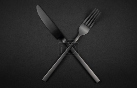 Photo for Black crossed fork and knife on dark background. Black silverware set - Royalty Free Image