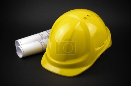 Photo for Yellow safety hard hat with engineering drawings on dark background - Royalty Free Image