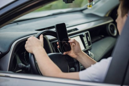 Casual driver guy distracted by his phone while in front of the steering wheel, using his smartphone with one hand while driving. Risk and danger situations on the road, violating traffic rule