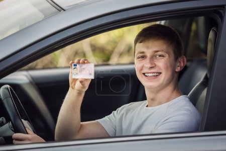 Foto de Tipo feliz y orgulloso mostrando su licencia de conducir por la ventana del coche - Imagen libre de derechos