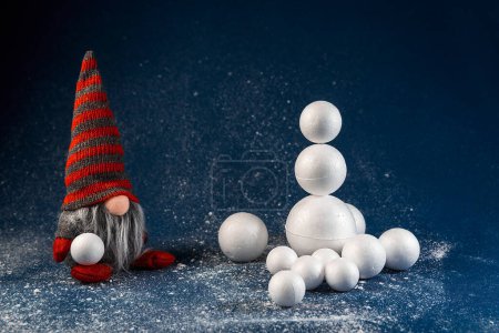 Téléchargez les photos : Décoration de Noël elfe, nain tenant boule de neige et construire bonhomme de neige. concept de délices d'hiver, scène de fond de vacances - en image libre de droit