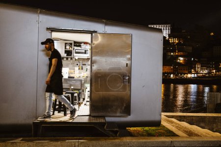 Téléchargez les photos : 17 avril 2023 - Porto, Portugal : Un travailleur quitte la cuisine dans un étal près de la rivière la nuit - en image libre de droit