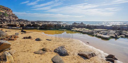 Photo for Pool of salt water on the rocky Headland at Point Arkwright with cloudy sky and a sunlit ocean. - Royalty Free Image