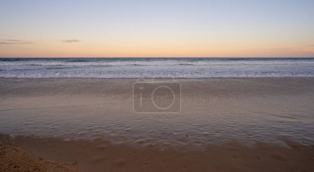 Téléchargez les photos : Regardant vers l'est au-dessus de l'océan Pacifique, Queensland, alors que le soleil se couche à l'ouest, attendant que la pleine lune se lève au-dessus de l'horizon tandis que les vagues de surf se brisent sur une plage de sable fin à Kawana, Sunshine Coast, une destination de vacances populaire. - en image libre de droit