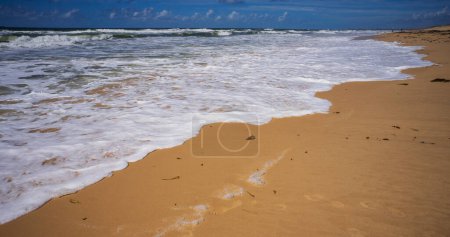 Dramatic background colours as the white wash or white foaming waves wash in onto a sandy beach on the Sunshine Coast at Kawana Queensland